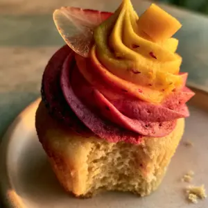 Close-up of a mango strawberry sunset cupcake with a bite missing showing the pale gold crumb.